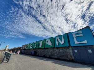 A picture showing the name of Folkstone at Folkstone Harbour Arm, a few people walking