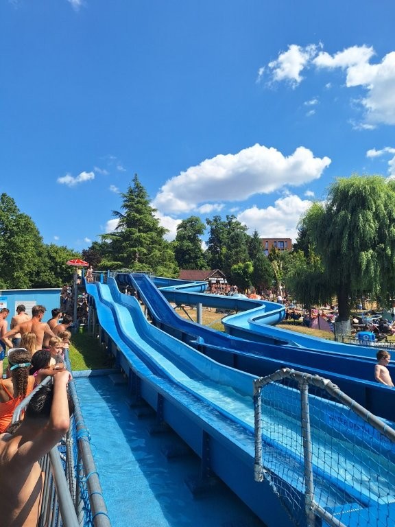 People waiting by the large blue water slides at Guildford Lido on a bright, sunny summer day.