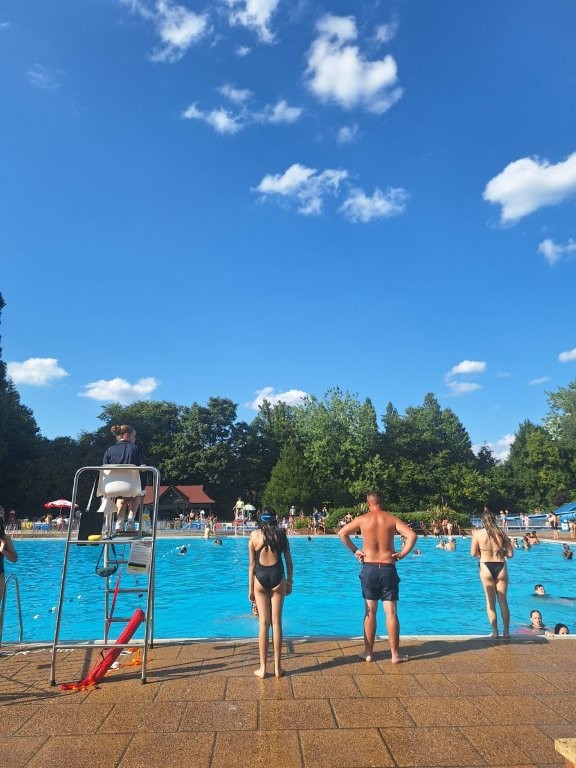Swimmers standing at the edge of the bright blue open-air pool at Guildford Lido on a sunny day.
